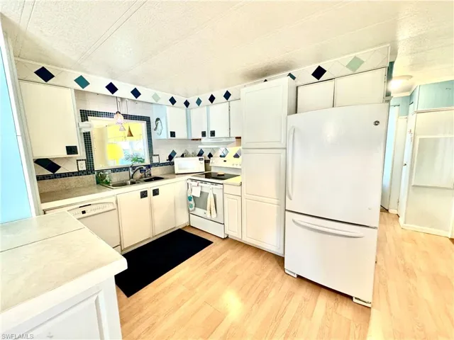 Kitchen with light hardwood / wood-style floors, white appliances, pendant lighting, sink, and white cabinets