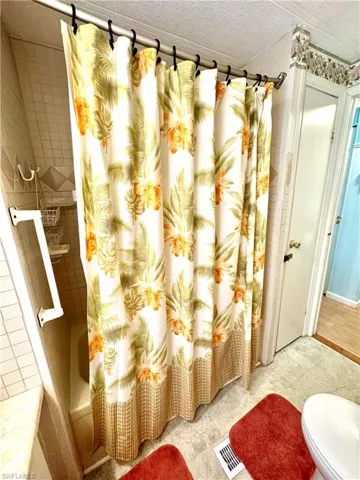 Bathroom featuring shower / bath combo with shower curtain, tile flooring, toilet, and a textured ceiling