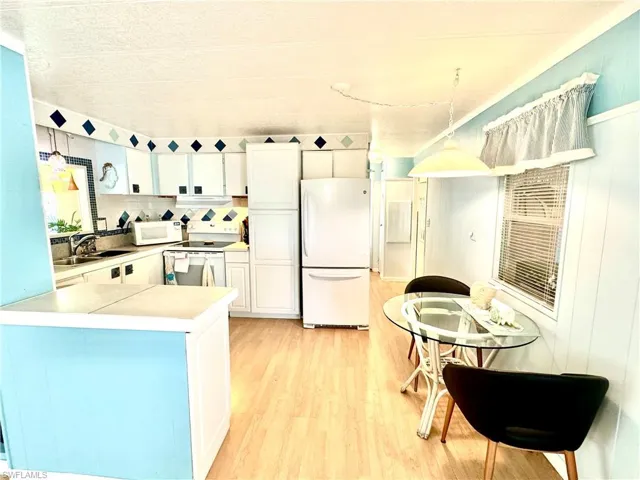 Kitchen with light hardwood / wood-style floors, kitchen peninsula, white appliances, pendant lighting, and sink