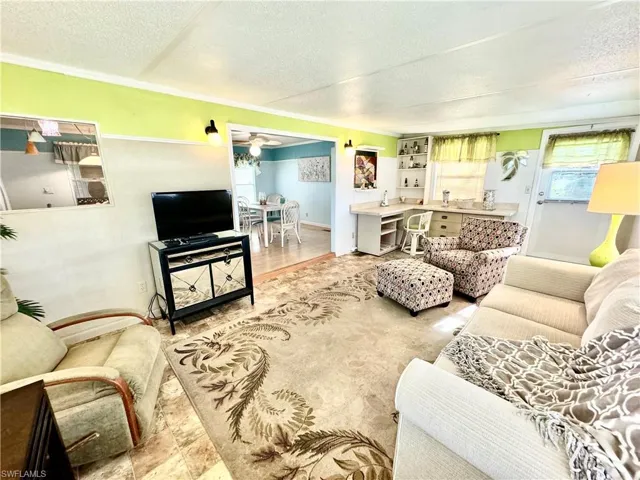 Living room featuring a textured ceiling, ornamental molding, wood-type flooring, and ceiling fan