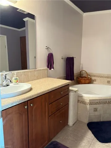 Bathroom with vanity, ornamental molding, a relaxing tiled tub, and tile patterned floors