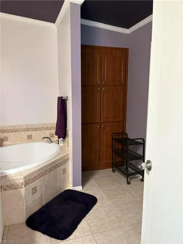 Bathroom with tile patterned floors, crown molding, and tiled tub