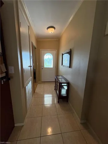 Doorway with crown molding and light tile patterned floors