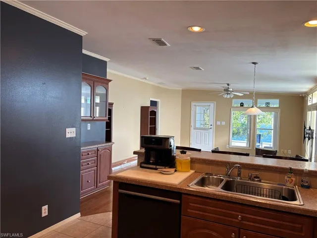 Kitchen with black dishwasher, sink, ceiling fan, ornamental molding, and light tile patterned floors