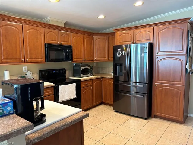 Kitchen with black appliances, crown molding, and light tile patterned floors