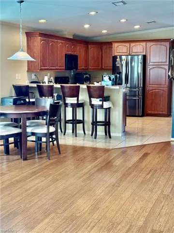 Kitchen featuring stainless steel refrigerator with ice dispenser, ornamental molding, a breakfast bar, pendant lighting, and light wood-type flooring