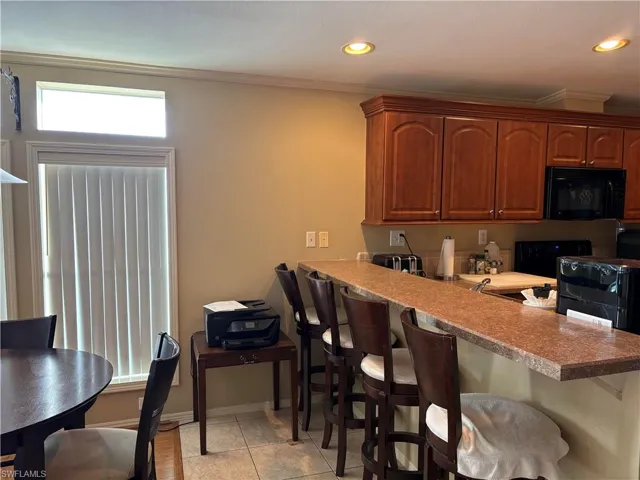 Kitchen featuring a kitchen breakfast bar, kitchen peninsula, black appliances, light tile patterned flooring, and crown molding