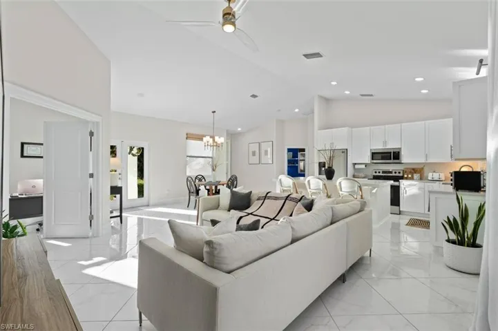Living room featuring high vaulted ceiling, recessed lighting, ceiling fan with notable chandelier, visible vents, and marble finish floor
