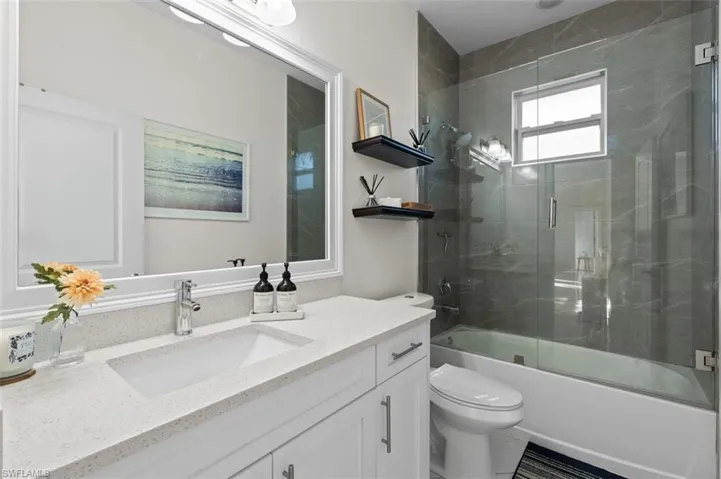 Bathroom with shower / bath combination with glass door, vanity, and toilet