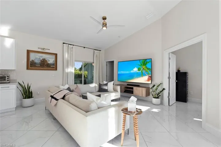 Living area featuring marble finish floor, baseboards, high vaulted ceiling, and a ceiling fan