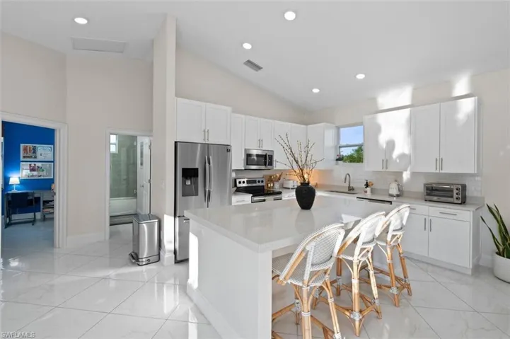 Kitchen featuring visible vents, a center island, stainless steel appliances, white cabinetry, and a sink