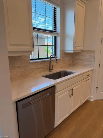Kitchenette featuring white shaker-style cabinetry, a stainless steel sink with a gooseneck faucet, light-toned countertop, and a light-colored tile backsplash