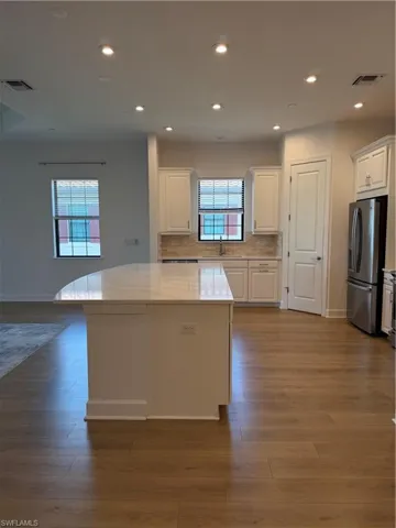 Modern kitchen featuring a large island with a light-toned countertop, ample white cabinetry, stainless steel appliances, and wood-finish flooring