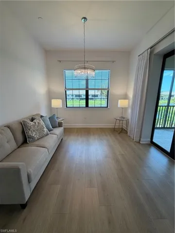 Spacious interior featuring wide-plank wood-finish flooring, a contemporary crystal chandelier, and a large window with blinds
