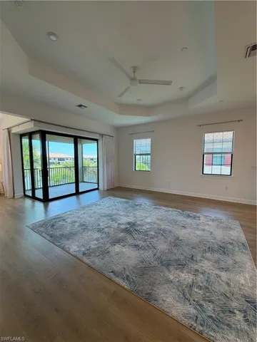 Spacious room featuring wood-finish flooring, a tray ceiling with a ceiling fan, and recessed lighting