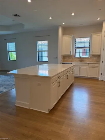 Kitchen featuring a large central island with a light-toned countertop, white cabinetry with dark hardware, a stainless steel sink, and a tiled backsplash