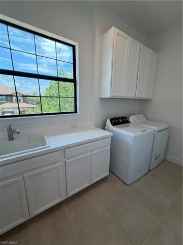 Dedicated laundry room featuring white cabinetry, a utility sink with a chrome faucet, and a large grid-pattern window