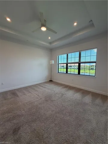 Spacious room featuring tray ceilings with recessed lighting, a contemporary ceiling fan, and carpeted flooring