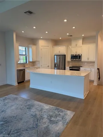 Open-concept kitchen featuring an expansive island with a light-toned countertop, white cabinetry, stainless steel appliances, and wood-finish flooring