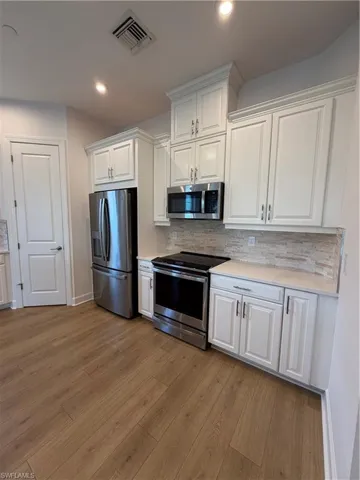 Modern kitchen with stainless steel appliances, white cabinetry, light-toned countertops, stone tile backsplash, and wood-finish flooring