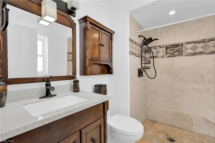 Bathroom with toilet, recessed lighting, a tile shower, and vanity