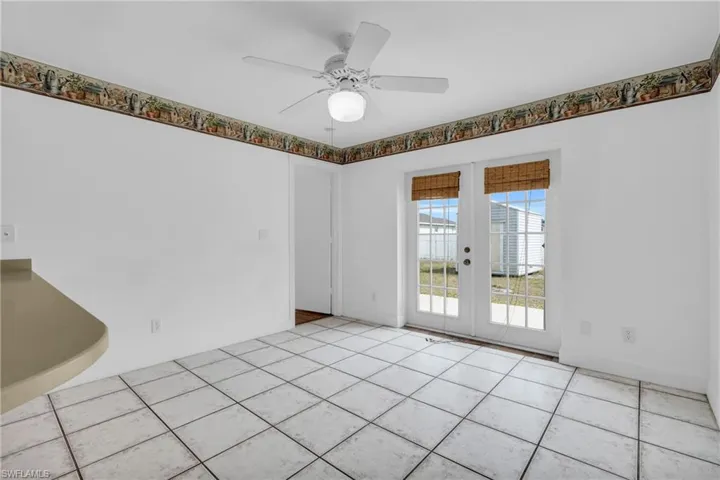 Empty room featuring light tile patterned floors, baseboards, a ceiling fan, and french doors