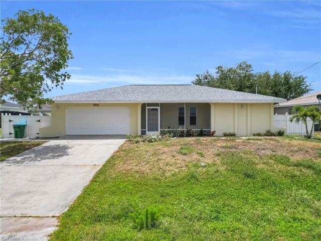 Ranch-style house with driveway, a front yard, a garage, fence, and stucco siding