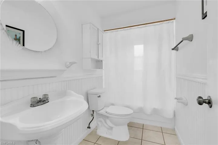 Bathroom featuring tile patterned floors, wainscoting, toilet, and shower / bath combination with curtain