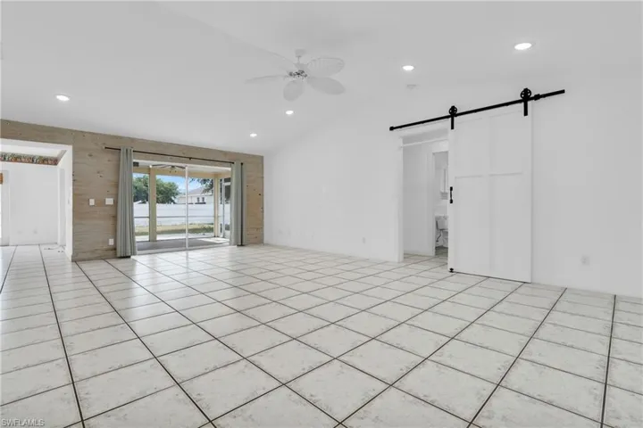 Unfurnished room featuring lofted ceiling, recessed lighting, a barn door, a ceiling fan, and light tile patterned floors