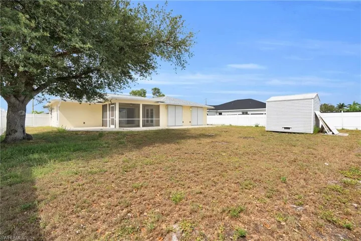 Rear view of house with a storage unit, a sunroom, a fenced backyard, an outbuilding, and a lawn