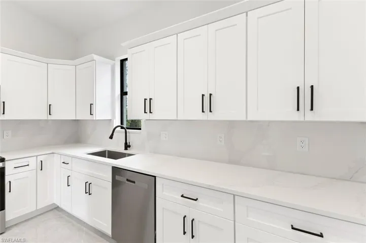 Kitchen featuring stainless steel dishwasher, tasteful backsplash, white cabinetry, light stone counters, and sink