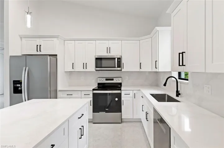 Kitchen featuring tasteful backsplash, appliances with stainless steel finishes, light tile patterned floors, sink, and lofted ceiling