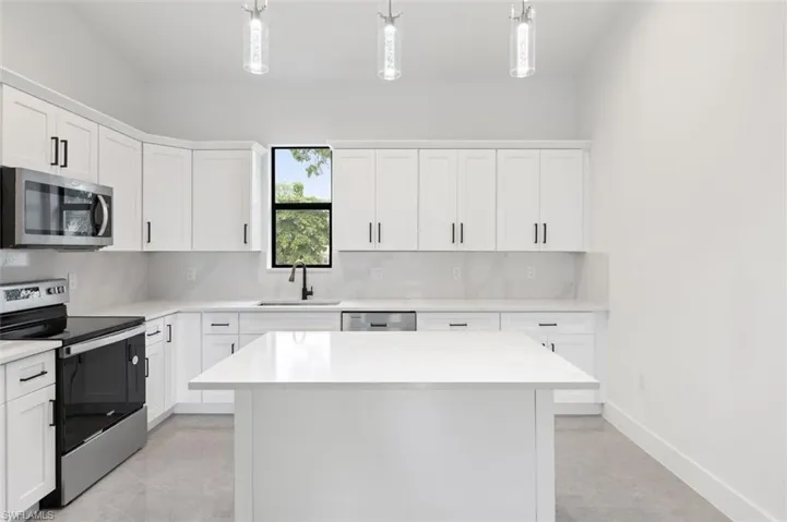 Kitchen featuring appliances with stainless steel finishes, decorative backsplash, sink, white cabinets, and hanging light fixtures