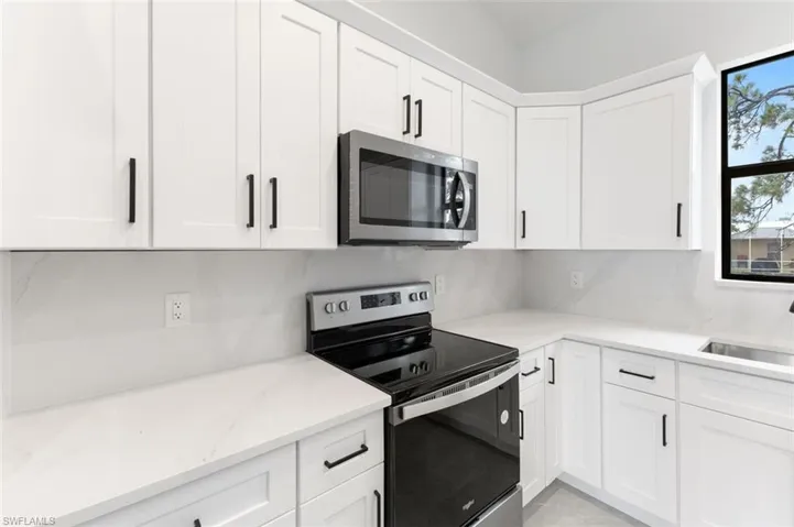 Kitchen with appliances with stainless steel finishes, decorative backsplash, white cabinetry, and light stone countertops