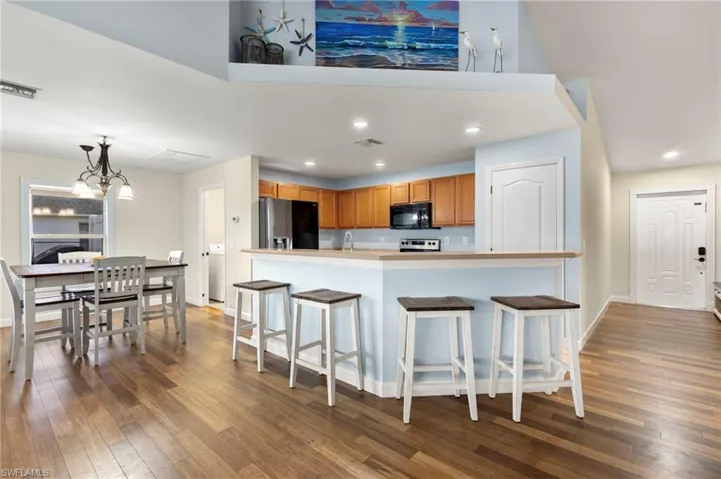 Kitchen featuring pendant lighting, hardwood / wood-style flooring, a kitchen bar, stainless steel fridge with ice dispenser, and a chandelier
