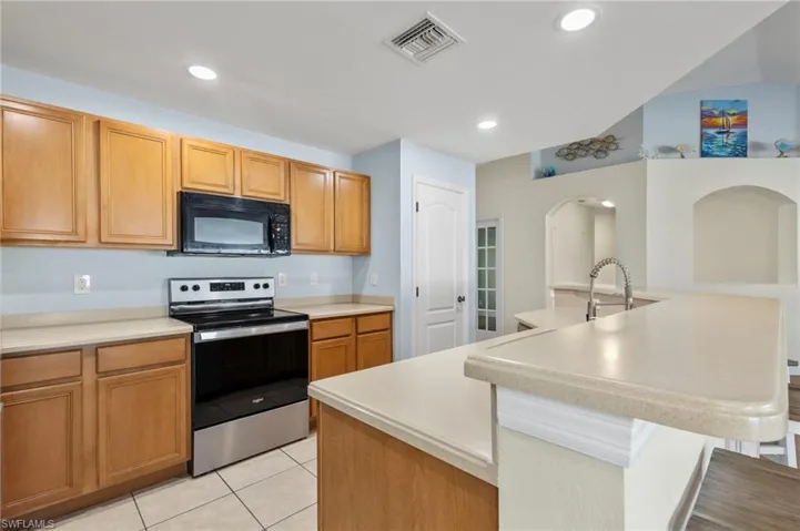 Kitchen with a kitchen breakfast bar, a kitchen island with sink, sink, light tile floors, and stainless steel electric range