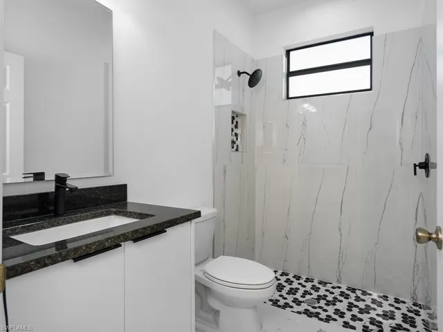Bathroom featuring tile patterned floors, vanity, a tile shower, and toilet