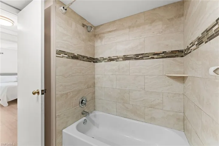 Recently Updated Bathtub with tiled surround, decorative mosaic accent band, and integrated shower head