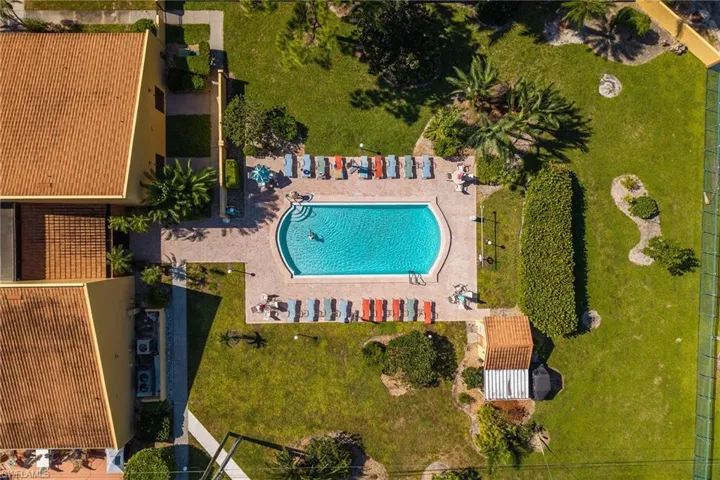 Resort-style pool with a paver deck, surrounded by expansive green space, mature landscaping, and a privacy hedge