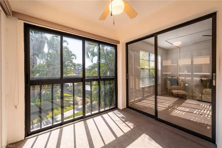 Sun-filled enclosed patio with a ceiling fan, black-framed sliding glass doors you can open for a nice gently breeze.