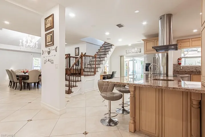 Kitchen with light stone counters, a chandelier, high quality fridge, island exhaust hood, and recessed lighting