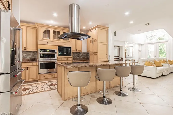 Kitchen with dark stone counters, island exhaust hood, appliances with stainless steel finishes, open floor plan, and light tile patterned flooring