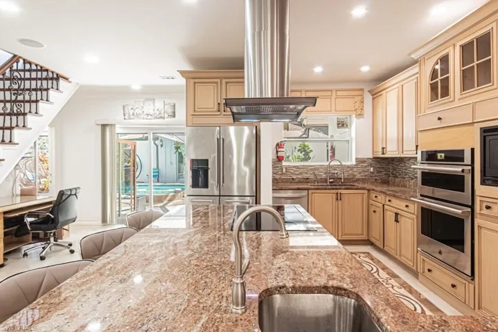 Kitchen featuring decorative backsplash, island range hood, dark stone countertops, a desk, and recessed lighting