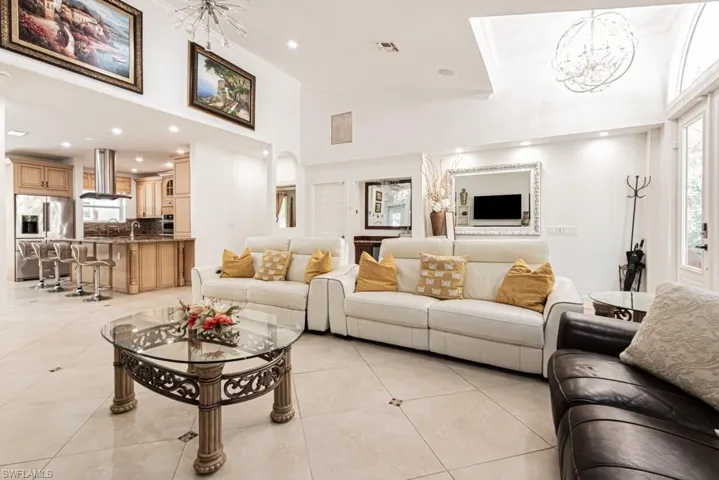 Living room with a chandelier, ornamental molding, high vaulted ceiling, recessed lighting, and light tile patterned floors