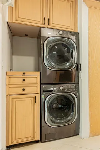 Laundry room featuring light tile patterned floors, stacked washer / drying machine, and cabinet space