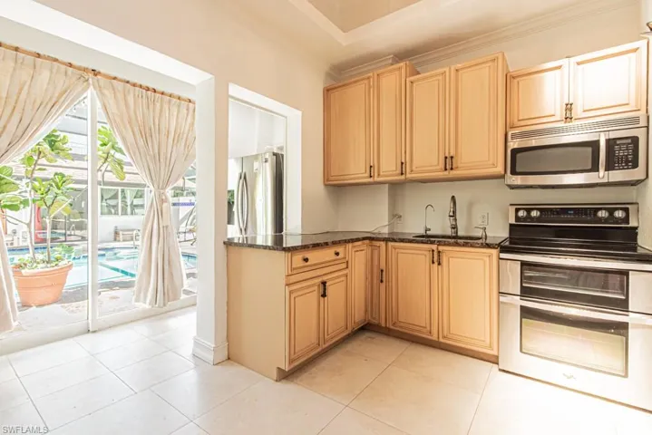 Guest House Kitchen featuring appliances with stainless steel finishes, dark stone counters, light tile patterned floors, light brown cabinets, and ornamental molding