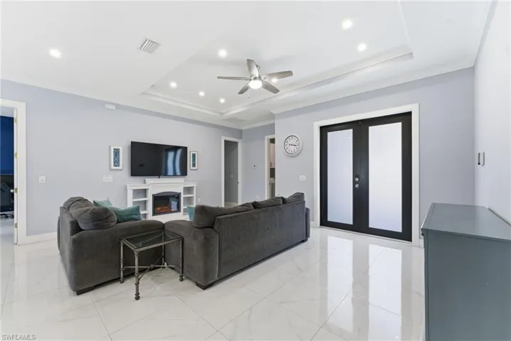 Living room featuring french doors, crown molding, ceiling fan, a warm lit fireplace, and a tray ceiling