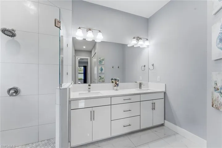 Full bathroom featuring double vanity, a tile shower, and light marble finish floors