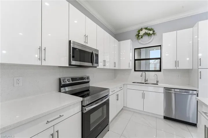 Kitchen with stainless steel appliances, tasteful backsplash, white cabinets, light marble finish floors, and crown molding