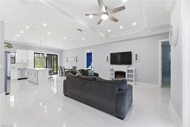 Living area with crown molding, a ceiling fan, recessed lighting, and a warm lit fireplace